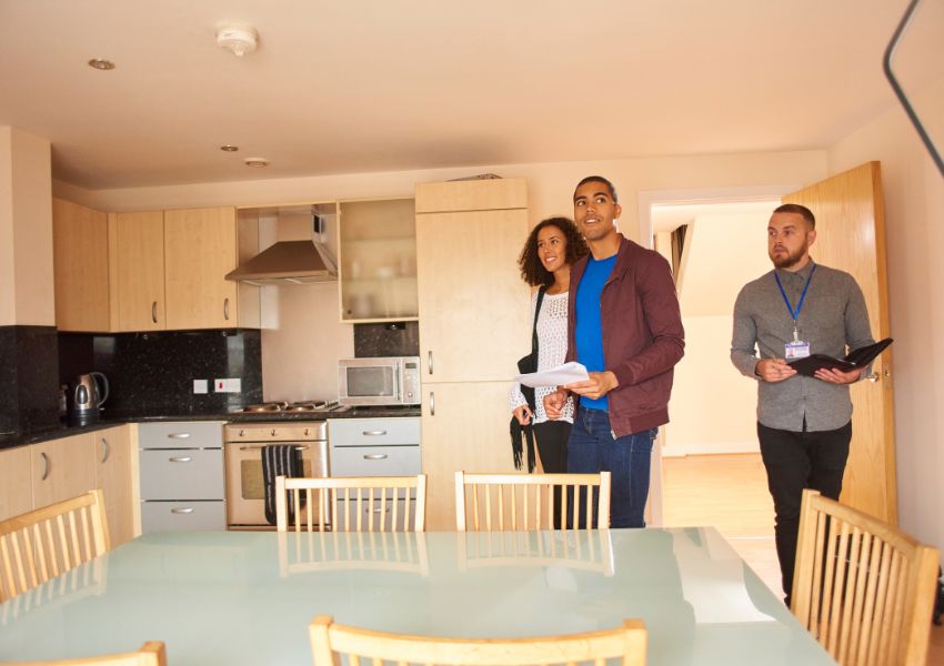 A property manager shows two tenants the inside of a rental unit kitchen.
